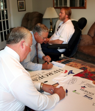 Charles County Commissioners Wayne Cooper and Samuel N. Graves, Jr., sign tee-shirts and signs for Michael White, Sr. (far right) at the recent “Heroes at Home Project” in Waldorf. 