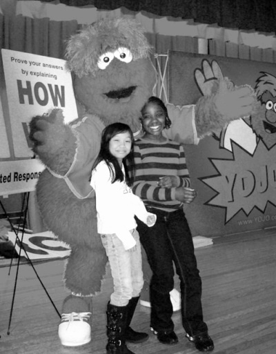 Dr. Gustavus Brown Elementary School fourth graders Hien Nguyen, left, and Destiny Bishop, right, pose with the cartoon character “YoJo,” who visited the school last month to share test-taking tips with students preparing for the Maryland School Assessment (MSA) tests. (Submitted photo)