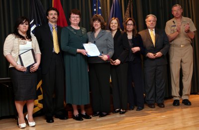 NAVSEA Commander Vice Adm. Kevin McCoy applauds the Telecommunications Audit Team after presenting them with the Total Ownership Cost Excellence Award. Team members (left to right) Juanita Brown, Rick Ballenger, Melody Belcher, Cheryl Feeser, Ann Shows, Rose Brubaker and Wayne Russell stand before the audience with Vice Adm. McCoy. (U.S. Navy photo by Laura Lakeway)