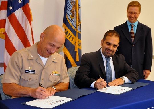 DAHLGREN, Va. (Sept. 7, 2016) - Capt. Brian Durant and Amit Kapoor sign an exclusive license agreement authorizing First Line Technology LLC to manufacture Navy patented lifesaving decontamination technology for warfighters and first responders. The 'Dahlgren Decon' decontamination solution - developed to defend U.S. troops against chemical, biological, and radiological agents - is protected under several patents by Naval Surface Warfare Center Dahlgren Division (NSWCDD). Durant, NSWCDD commanding officer, and Kapoor, First Line Technology president, emphasized the importance of the technology transfer that will equip first responders across the nation with technology to defend the public from hazardous threats. "This is the home run of technology transfer and doesn't happen without a lot of contributors," said Chris Hodge, NSWCDD scientist and Dahlgren Decon inventor, standing. Hodge and his team worked for more than a decade to develop and test this revolutionary response to chemical and biological warfare agents. (U.S. Navy photo/ Released)