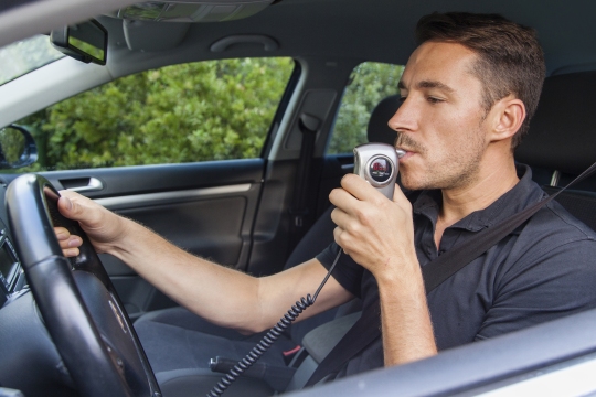 Stock photo of a man blowing into an in-car breathalyzer, otherwise known as an ignition interlock device.