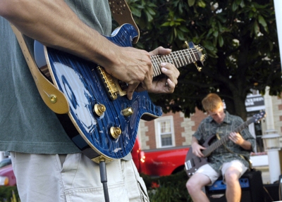 Zach Werrell lays down a bass line in the background. Partially shown in the foreground, mentor Bob Schaller leads the Guitar Club as they play on the town square in Leonardtown, Md. Photo Courtesy CSM.
