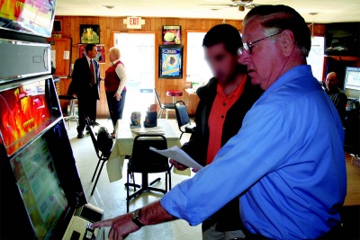 Brass Rail owner Charles Gatton demonstrates the operation of an electronic gaming machine to a Southern Maryland Information Center intelligence officer during last week’s information gathering operation on gambling devices operating in the county. (Photo: Guy Leonard, County Times)